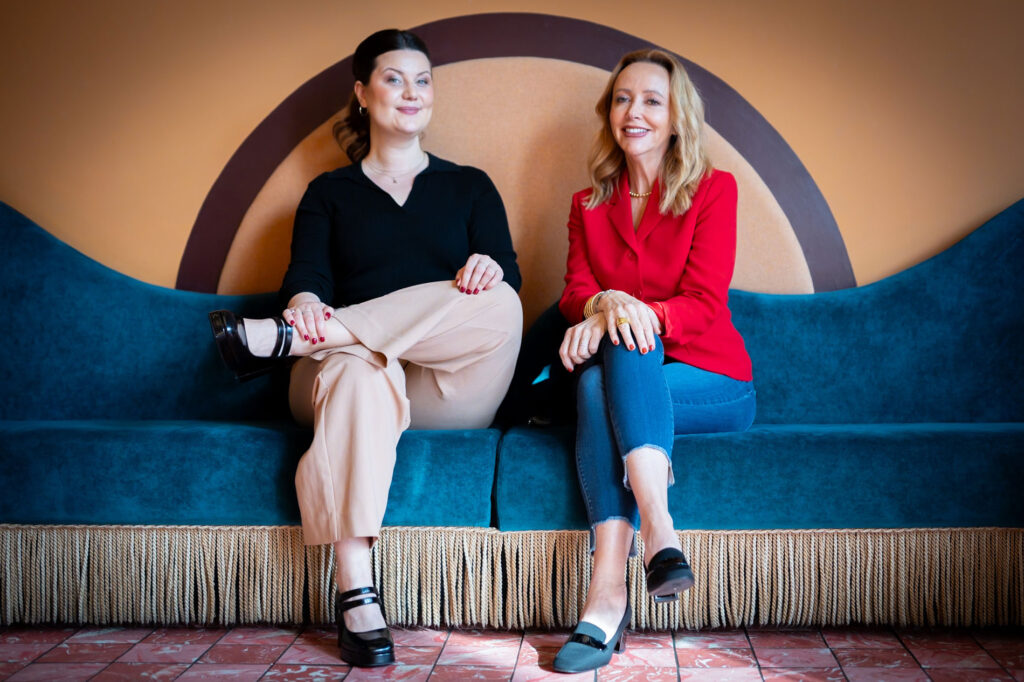 Kaitlin Wilkes and Kristine Bochino on a blue sofa smiling